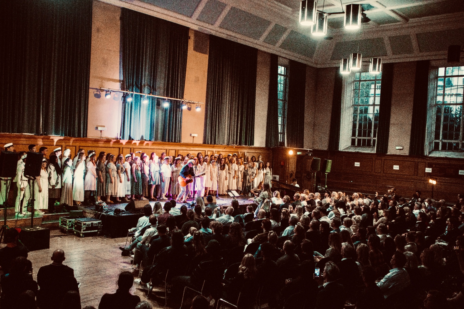The LondonSwedes Choir performing on stage at the annual Valborg concert in a grand hall with a guest guitarist and full audience